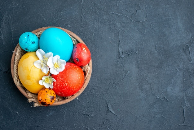 Vista de cima ovos de páscoa coloridos dentro do prato na superfície escura