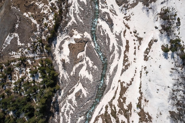 Vista de cima para baixo do rio sinuoso da montanha que flui através do padrão de derretimento da neve Cáucaso Rússia