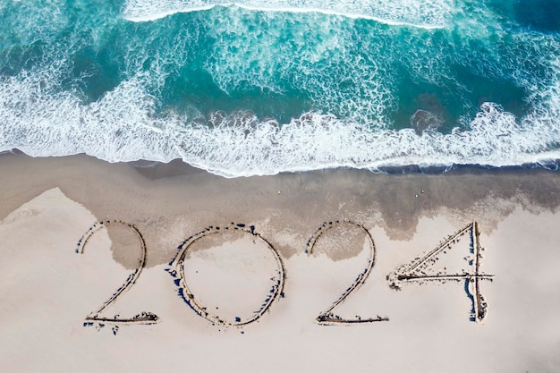 Vista de cima para baixo dos números do ano novo de 2024 escritos na areia do litoral