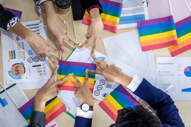 Foto vista de cima trabalhadores bem-sucedidos grupo de parceiros de negócios asiáticos com diversos gêneros (lgbt), juntando as mãos com a bandeira lgbt de papel em reunião na sala do escritório,