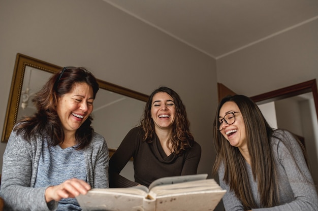 Vista de cima três mulheres, mãe e filhas, olhando um livro de memórias e rindo. União, conceito de família.