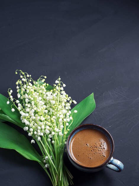 Vista de cima uma xícara de café expresso em uma mesa de concreto preto e um buquê de flores de maio de lírios do vale