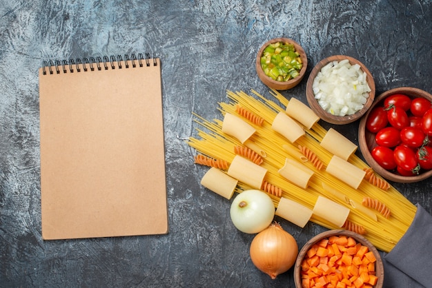 vista de cima várias massas rigatoni espaguete espirais caderno vegetais picados em tigelas sobre fundo cinza