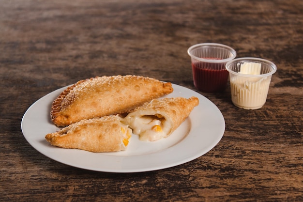 Vista de close-up de empanadas latino-americanas de milho e queijo frito com coberturas em cima de uma mesa de madeira