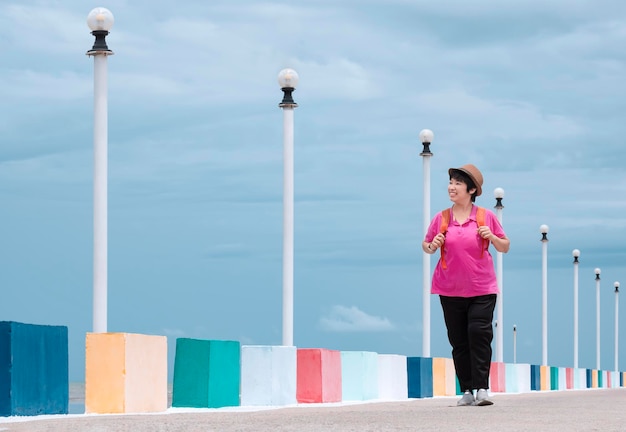 Vista de corpo inteiro de uma turista asiática feliz andando na ponte multicolorida no ponto de vista do mar