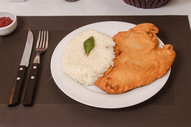 Vista de detalhe de arroz com milanesa servido em um prato sobre uma mesa branca