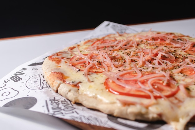 Vista de detalhe de uma pizza com tomate e presunto fatiado em uma mesa branca