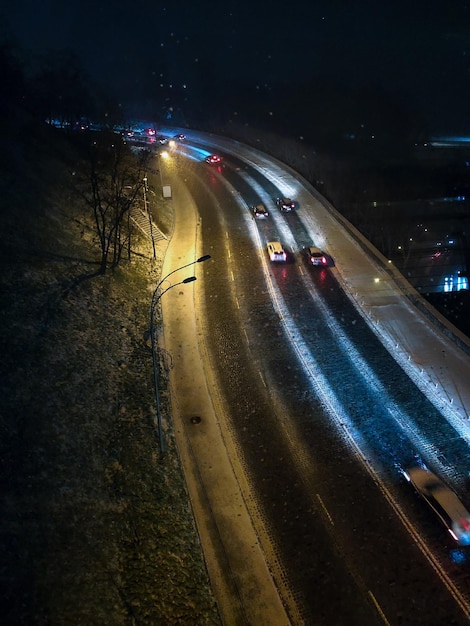 Vista de drone da estrada noturna de inverno com árvores e carros passando abaixo