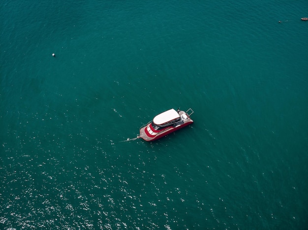 Vista de drone da pequena lancha vermelha e branca novinha em folha no mar azul, brilha no sol brilhante; conceito de navios.