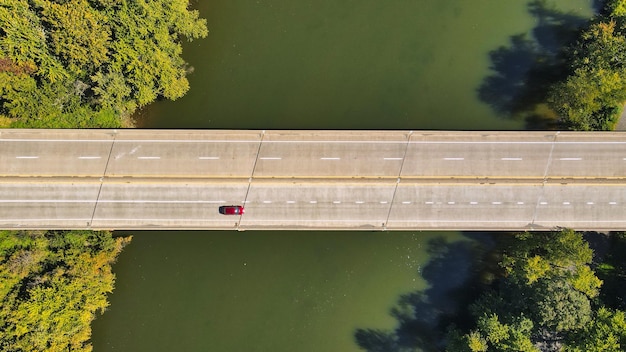 Vista de drone de um carro dirigindo em uma ponte rodoviária sobre um rio cercado por vegetação