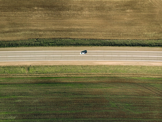 Vista de drone de uma estrada estreita entre dois campos cultivados. O único carro dirigindo na estrada