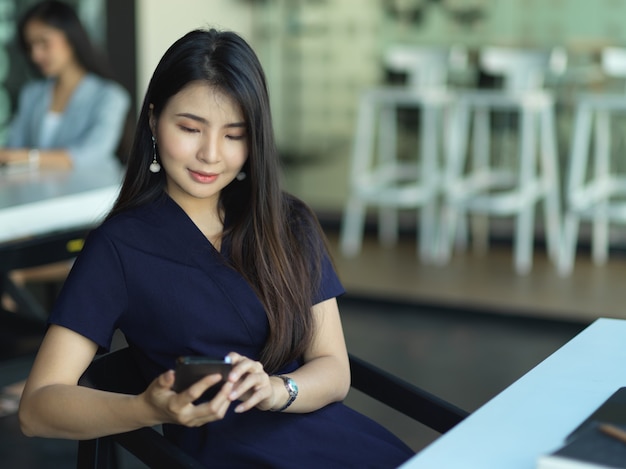 Vista de empresária usando smartphone enquanto relaxa no refeitório