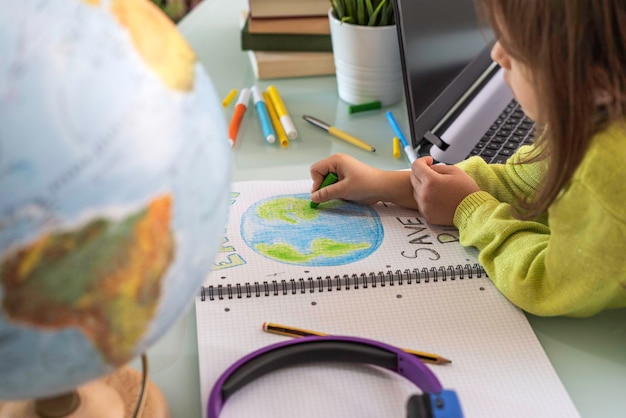 Foto vista de grande angular da menina criança desenha o planeta terra com cores de cera no caderno escolar para o dia da terra menina ativista escreve a mensagem salve o planeta proteção do aquecimento global do meio ambiente