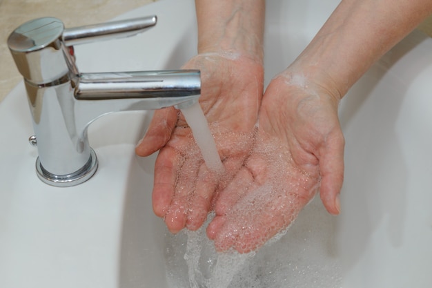Foto vista de mãos femininas em espuma com sabão em close-up de água da torneira