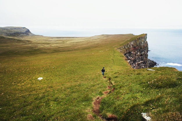 vista de penhascos de pássaros da Islândia em grama verde Oceano Atlântico Norte mulher turista andando Latrabjarg