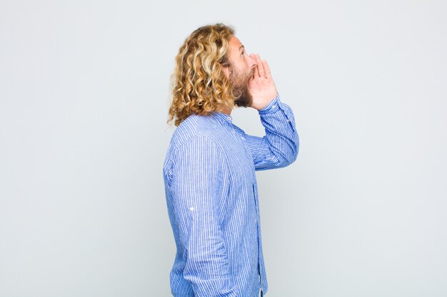 Vista de perfil de homem loiro, parecendo feliz e animado, gritando e chamando para copiar o espaço na lateral