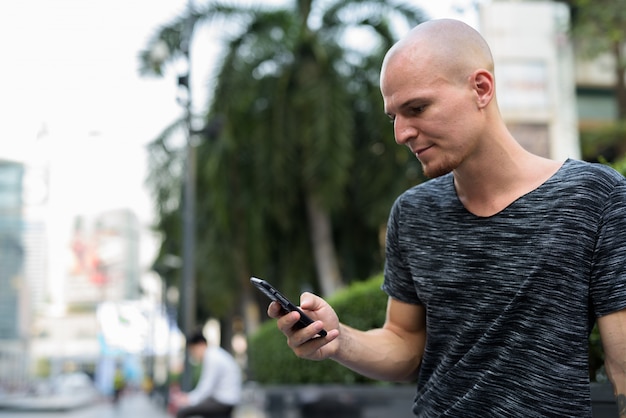 Vista de perfil de jovem bonito careca usando telefone celular