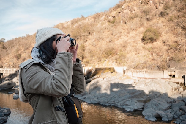 vista de perfil de jovem fotógrafa mulher em uma montanha caminhando e tirando fotos das paisagens