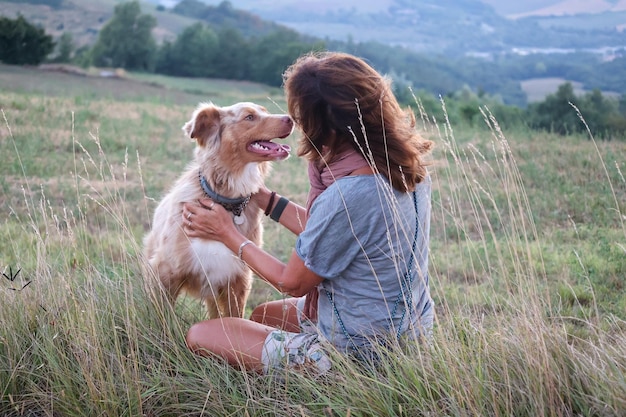 Foto vista de perfil de mulher sentada em um campo brincando com seu cão pastor australiano