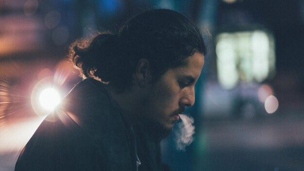 Vista de perfil de um homem fumando na cidade à noite
