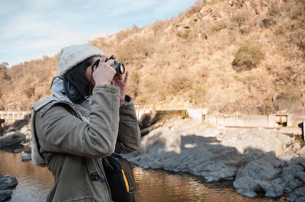 Vista de perfil de uma jovem fotógrafa em uma montanha caminhando e tirando fotos das paisagens
