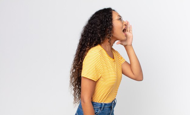 Vista de perfil de uma linda mulher hispânica, parecendo feliz e animada, gritando e chamando para copiar o espaço ao lado