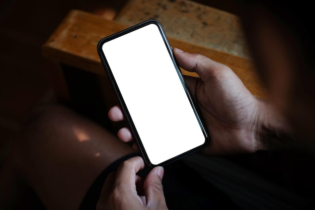 Vista de perto as mãos do jovem segurando a tela vazia do smartphone enquanto está sentado no local de trabalho