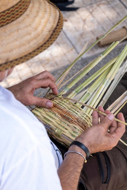 Foto vista de perto das mãos de um homem tecendo uma cesta de vime de canário