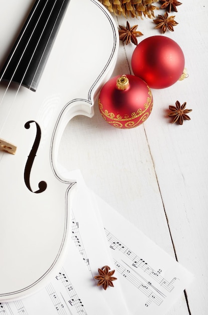 Foto vista de perto de notas musicais de violino e bolas vermelhas de decoração de natal na mesa de madeira branca