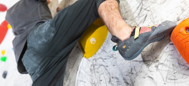 Foto vista de perto de um jovem ou de um alpinista com sapatos de escalada em uma parede interior artificial em uma escalada c