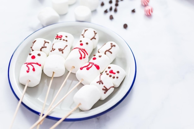 Vista de perto. Fazendo boneco de neve de marshmallow e renas em palitos para chocolate quente e bebidas de cacau.