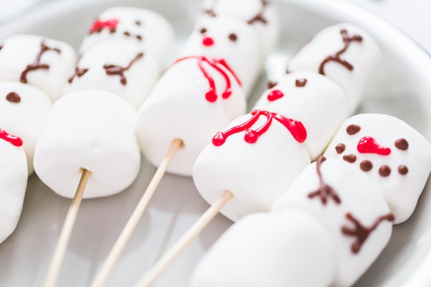 Vista de perto. Fazendo boneco de neve de marshmallow e renas em palitos para chocolate quente e bebidas de cacau.