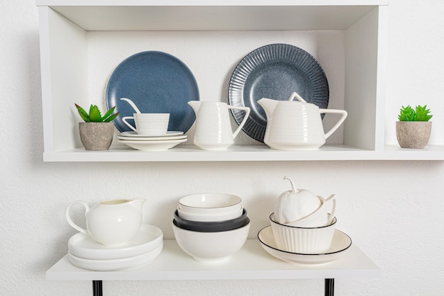 Vista de primeiro plano de prateleiras de cozinha abertas com porcelana e utensílios de cerâmica fundo de cozinha elegante em tons de branco