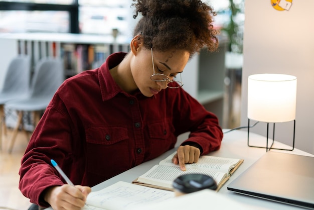 Vista de retrato de alto ângulo de um jovem estudante multirracial moreno muito ocupado sentado à mesa e escrevendo algo no caderno