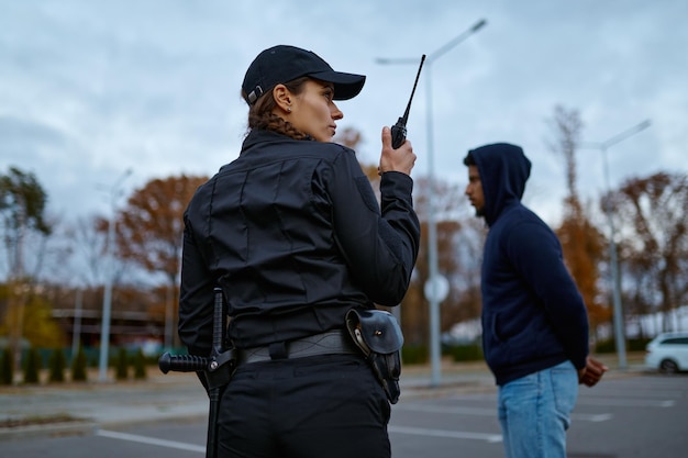 Vista de trás da mulher policial de uniforme usando rádio portátil para comunicação policial