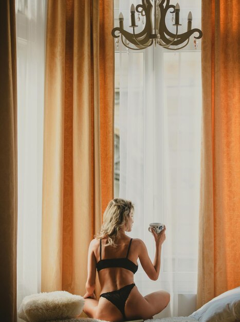 Vista de trás de mulheres jovens e saudáveis no quarto bebendo café pela manhã, jovem e sensual mulher relaxada