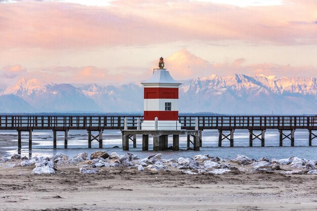 Vista de um farol e as montanhas cobertas de neve ao fundo em Giulia Itália