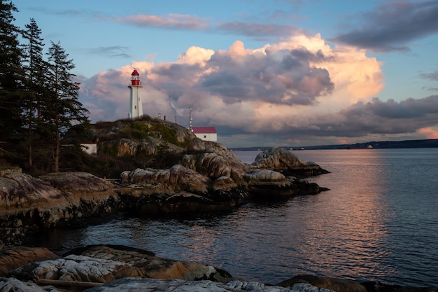 Vista de um farol em uma costa rochosa durante um pôr do sol nublado