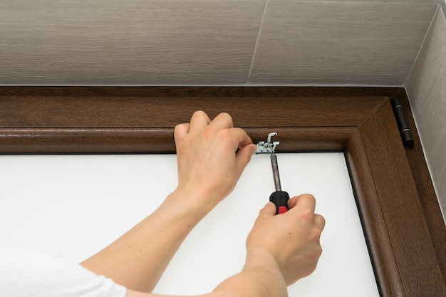 Vista de um homem apertando um parafuso em uma janela de plástico marrom montando uma persiana em uma janela de plástico marrom