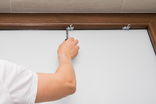 Vista de um homem apertando um parafuso em uma janela de plástico marrom montando uma persiana em uma janela de plástico marrom