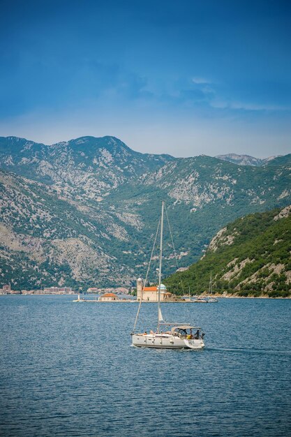 Vista de um iate branco flutuante em direção a Nossa Senhora das Rochas na Baía de Kotor