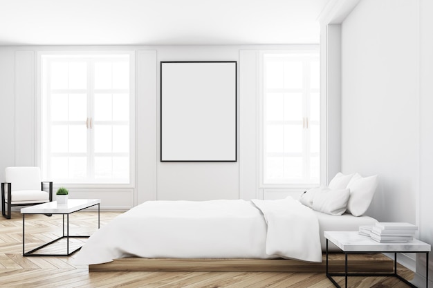 Vista de um interior de quarto branco com uma cama dupla, uma mesa de café, uma parede em branco e uma imagem vertical sobre ele.