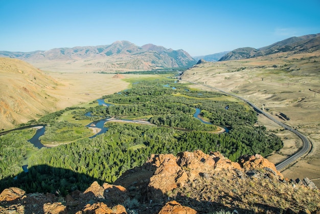 Vista de um vale de montanha verde entre encostas secas, meandros do rio