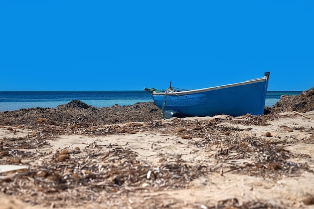 Vista de um velho barco de madeira na areia branca da costa mediterrânea. Descanse no mar na Ilha Djerba, Tunísia