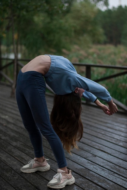 Foto vista de uma garota com corpo atlético em traje de ginástica está fazendo exercícios no parque em tempo nublado e chuvoso xa