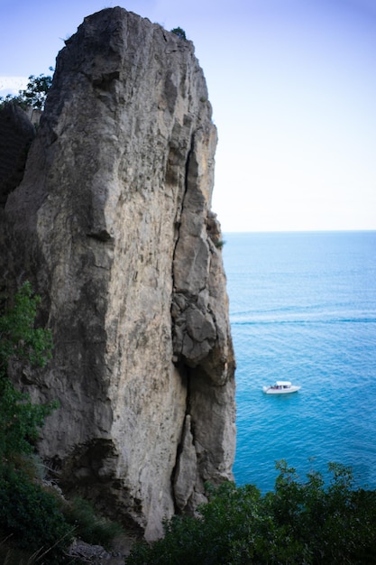 Vista de uma rocha não criminosa e do mar com um pequeno barco à distância a escala da natureza