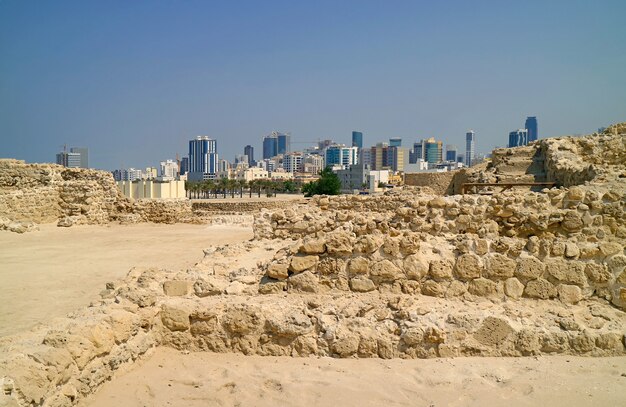 Vista deslumbrante do Forte do Bahrein ou das ruínas da estrutura Qal'at al-Bahrain com a moderna paisagem urbana de Manama no pano de fundo, Bahrein