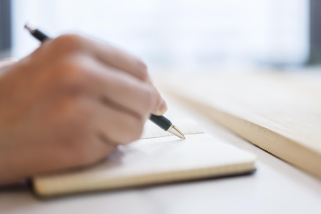 Vista detallada de la mano de un hombre escribiendo notas en un bloc de notas con un fondo borroso