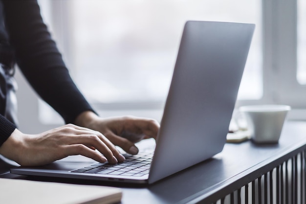 Vista detallada de las manos de una mujer escribiendo en un elegante entorno de oficina con teclado portátil suavemente borroso en el fondo