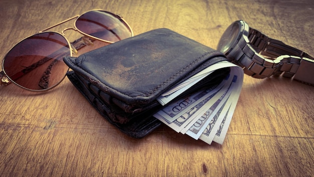 Foto vista directa de una billetera vieja con billetes de banco gafas de sol y fondo de reloj